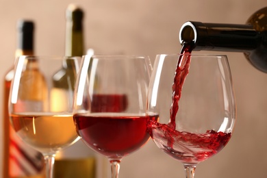 Pouring wine from bottle into glass on blurred background, closeup