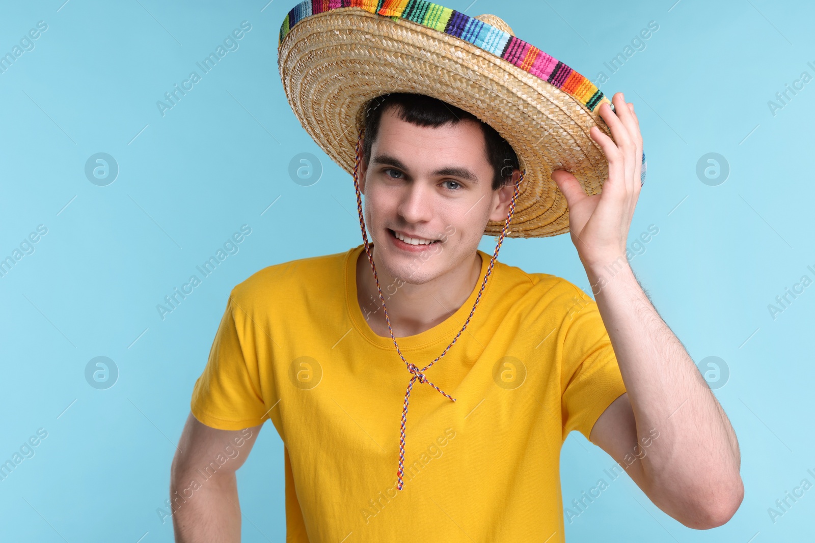 Photo of Young man in Mexican sombrero hat on light blue background