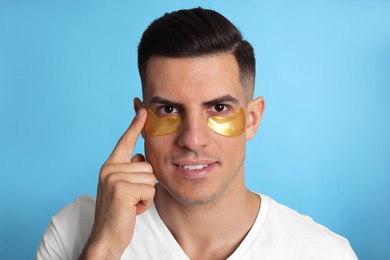 Man applying golden under eye patch on light blue background