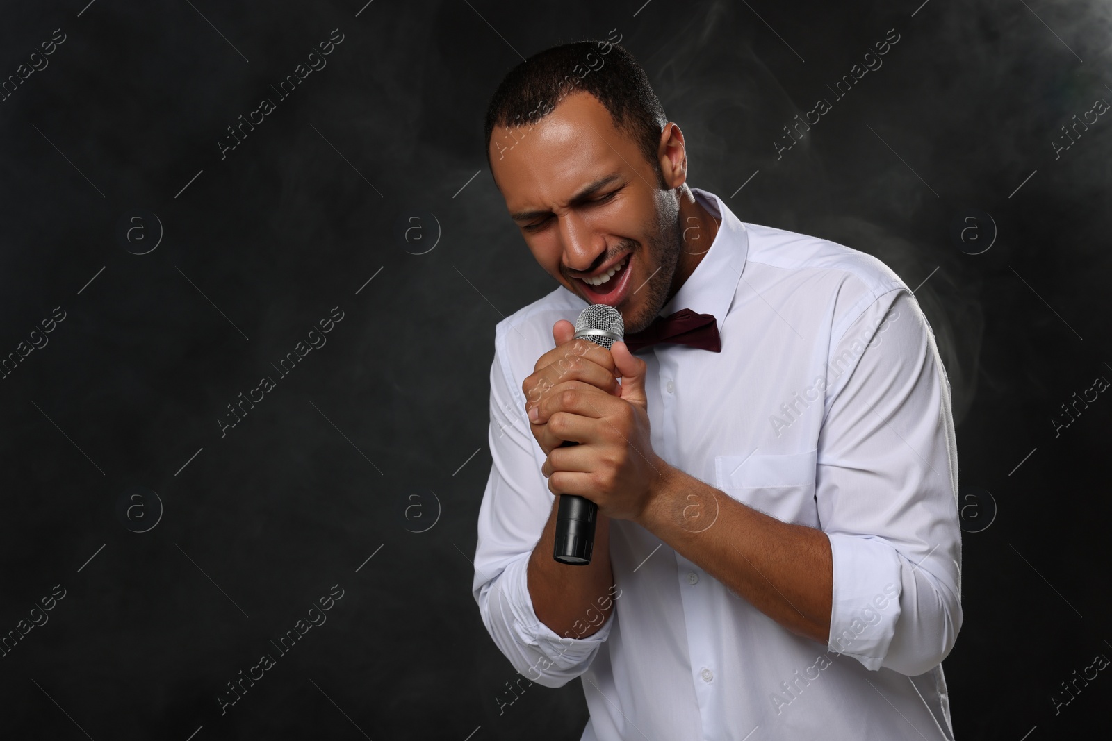 Photo of Handsome man with microphone singing on black background. Space for text