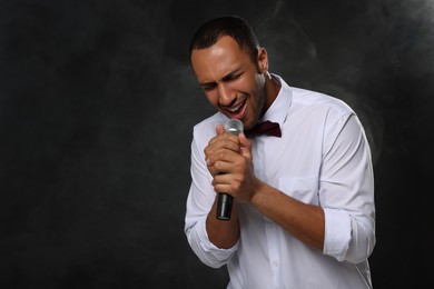 Photo of Handsome man with microphone singing on black background. Space for text
