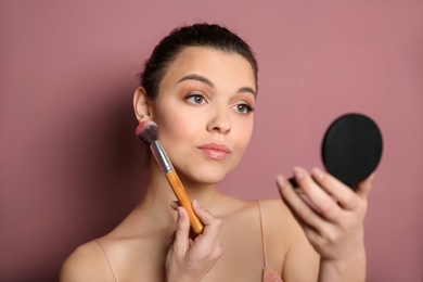 Young woman applying makeup on color background. Professional cosmetic products