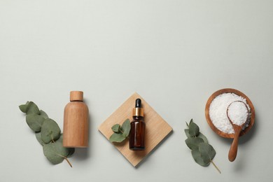 Aromatherapy products. Bottles of essential oil, sea salt and eucalyptus leaves on grey background, flat lay