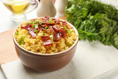 Photo of Tasty millet porridge with bacon and green onion in bowl on table, closeup