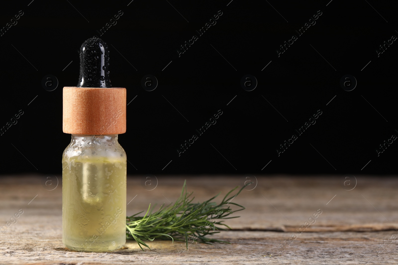 Photo of Bottle of essential oil and fresh dill on wooden table against black background, space for text