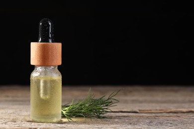 Bottle of essential oil and fresh dill on wooden table against black background, space for text