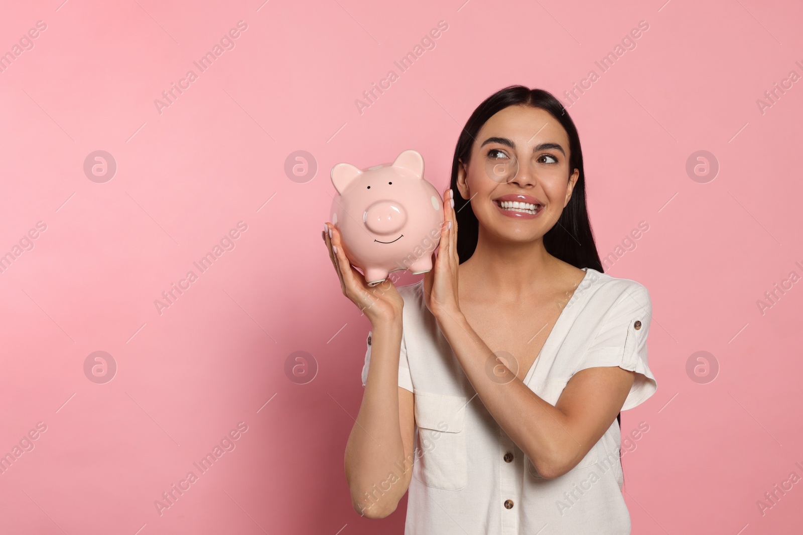 Photo of Happy young woman with ceramic piggy bank on pale pink background, space for text