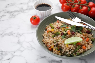 Photo of Tasty fried rice with vegetables served on white marble table, closeup. Space for text