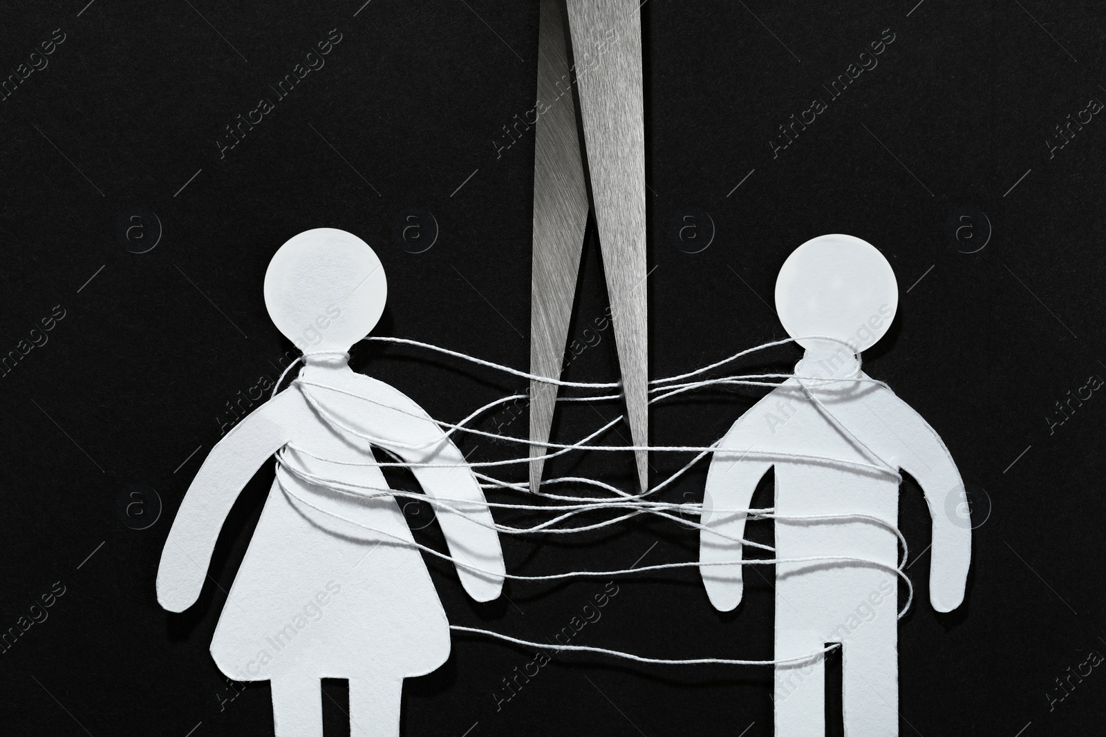 Photo of Divorce concept. Paper human figures with white thread and scissors on black background, flat lay
