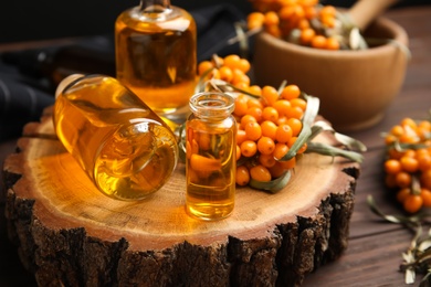 Photo of Natural sea buckthorn oil and fresh berries on wooden table, closeup
