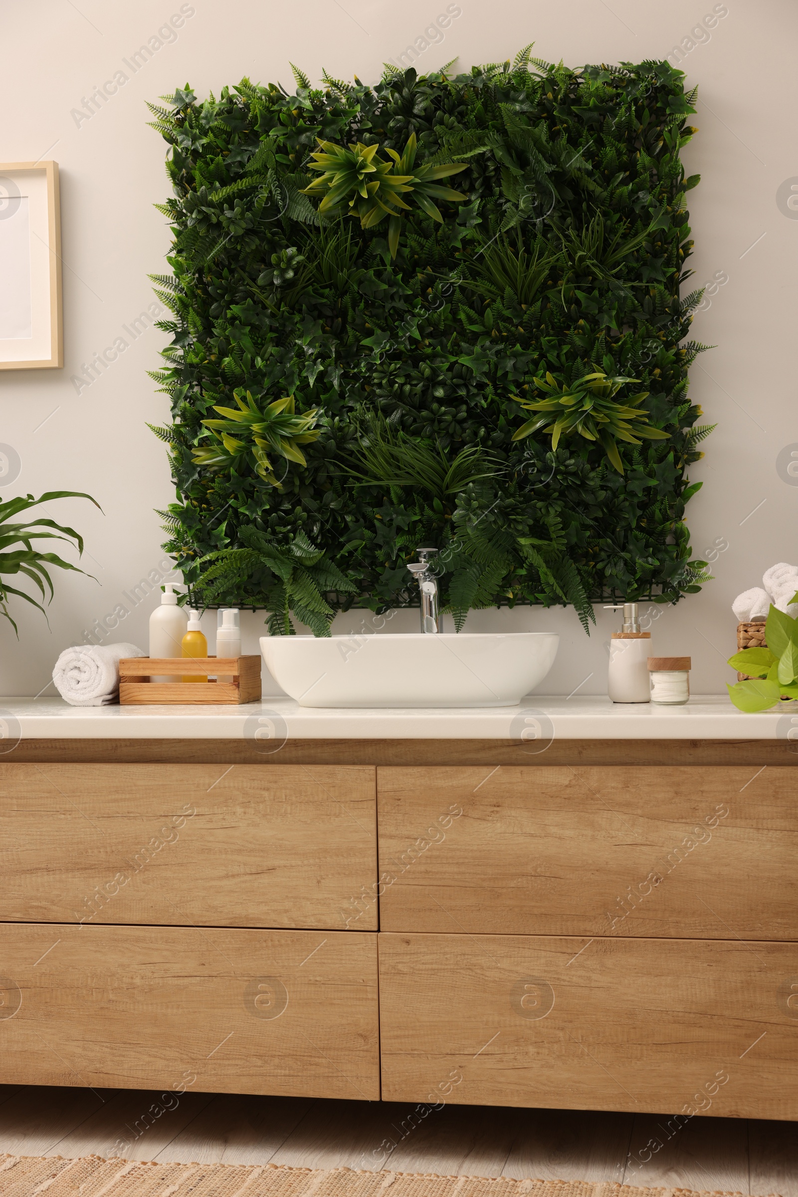 Photo of Green artificial plants, vanity and different personal care products in bathroom