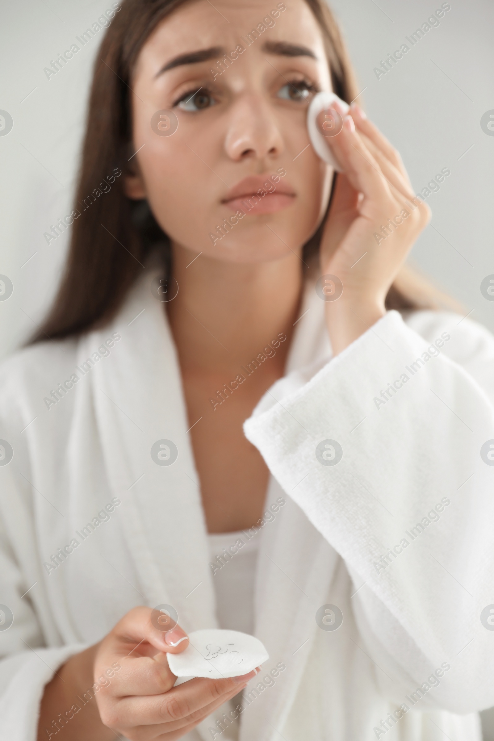 Photo of Young woman with eyelash loss problem removing makeup indoors