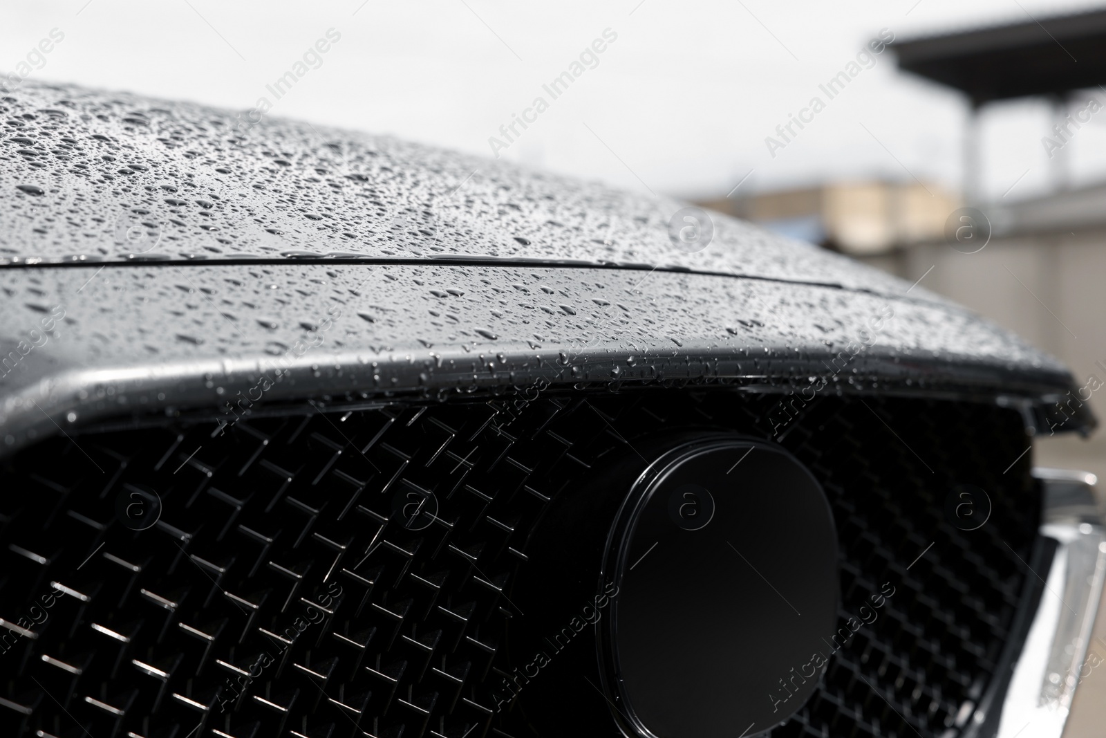 Photo of Front part of modern car in water drops outdoors, closeup