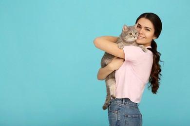 Young woman with adorable cat on light blue background, space for text