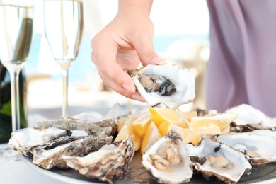 Photo of Woman holding fresh oyster over plate, focus on hand
