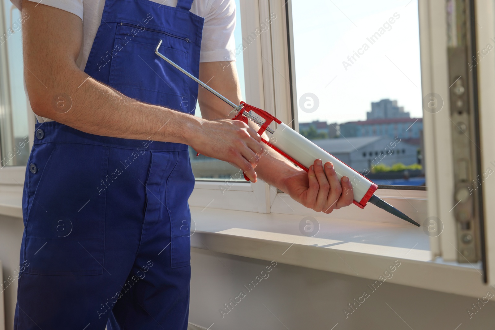 Photo of Worker sealing plastic window with caulk indoors, closeup. Installation process