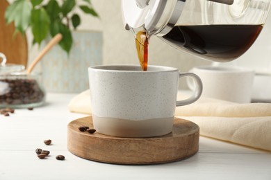 Photo of Pouring coffee into cup at white wooden table, closeup