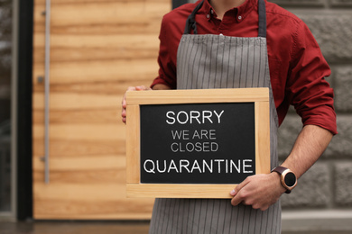 Image of Business owner holding sign with text SORRY WE ARE CLOSED QUARANTINE near his cafe, closeup