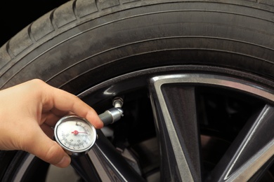 Photo of Man measuring car tire pressure with air gauge, closeup. Safety control