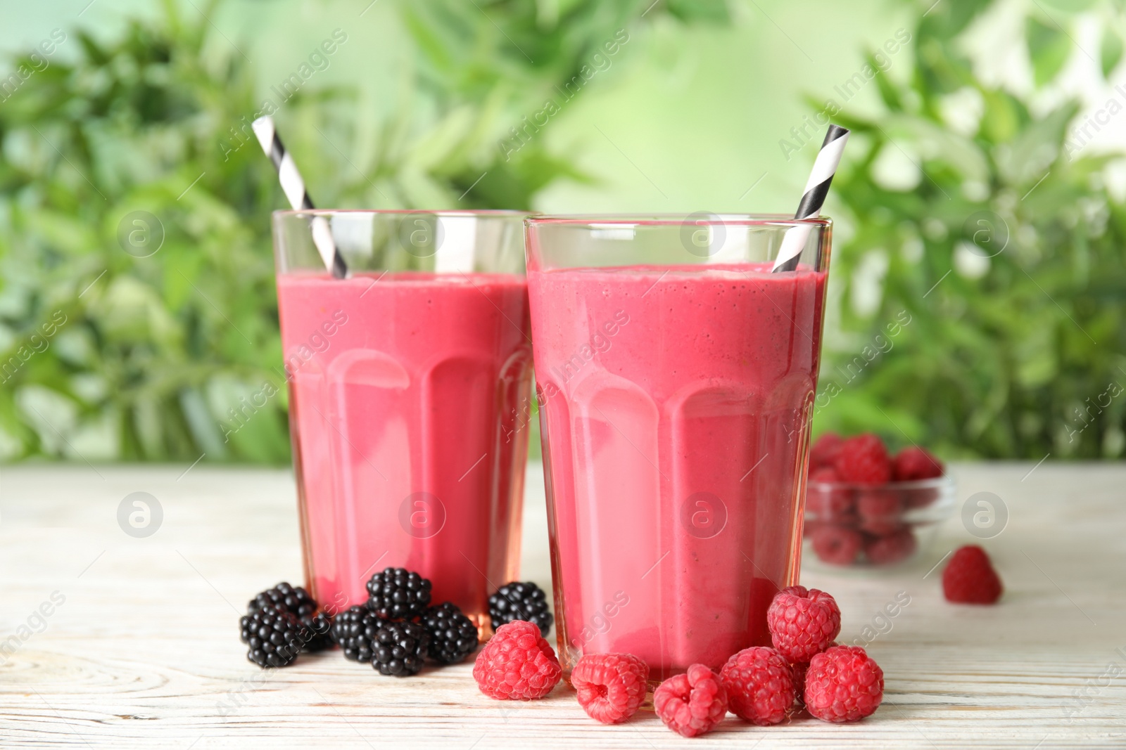 Photo of Tasty fresh milk shakes with berries on white wooden table against blurred background