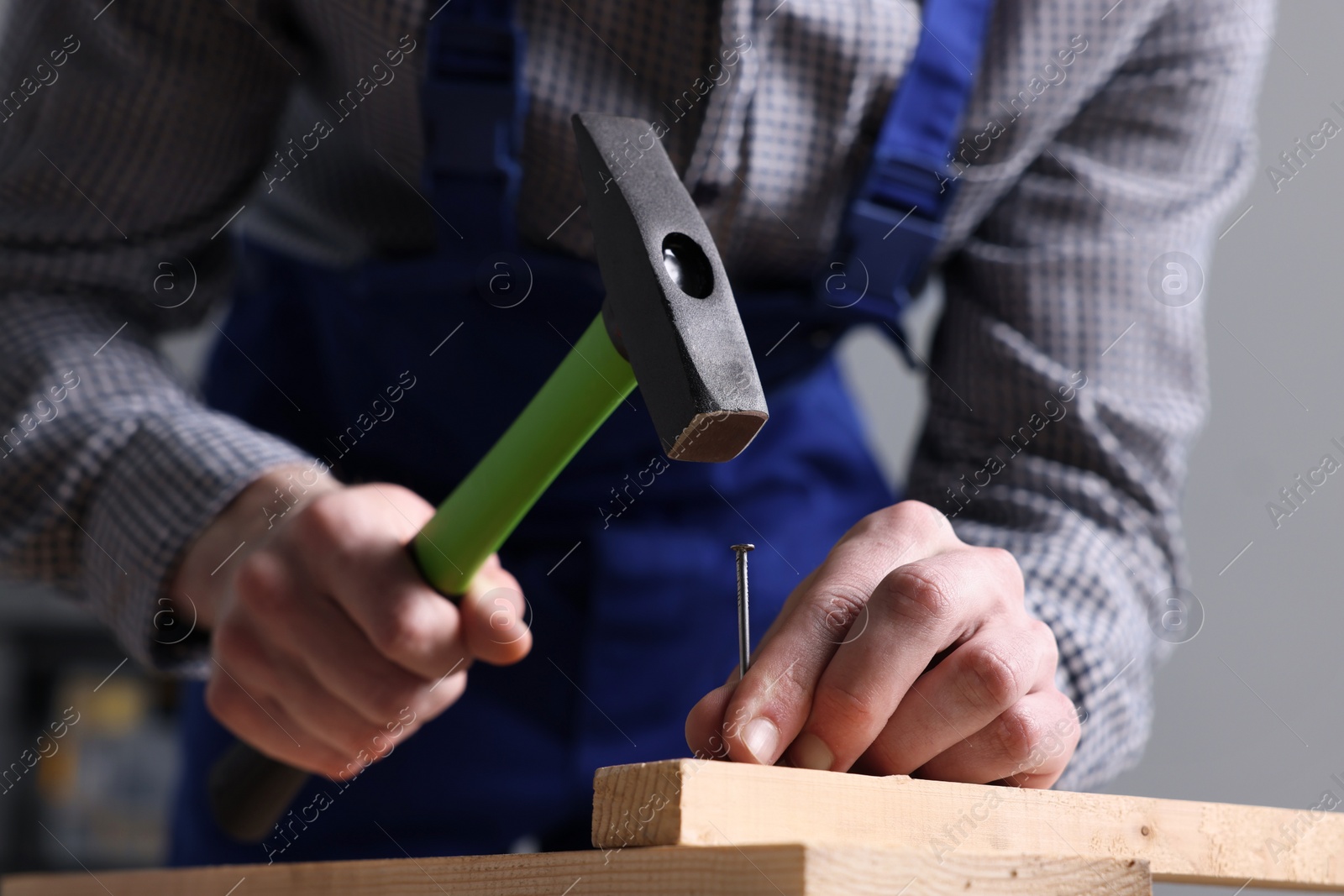 Photo of Professional repairman hammering nail into board at wooden table indoors, closeup