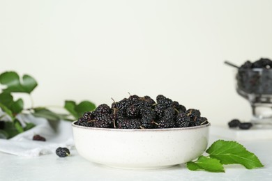 Photo of Bowl of delicious ripe black mulberries on white table, space for text
