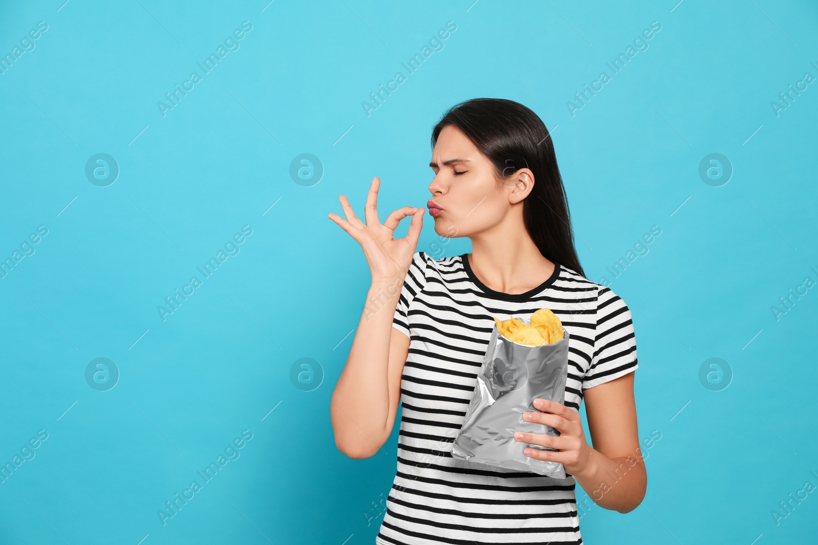 Photo of Beautiful woman eating potato chips on light blue background. Space for text