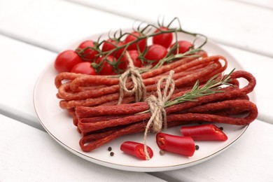 Photo of Bundles of delicious kabanosy with rosemary, peppercorn, chilli and tomatoes on white wooden table