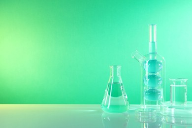 Laboratory analysis. Different glassware on table against green background, space for text