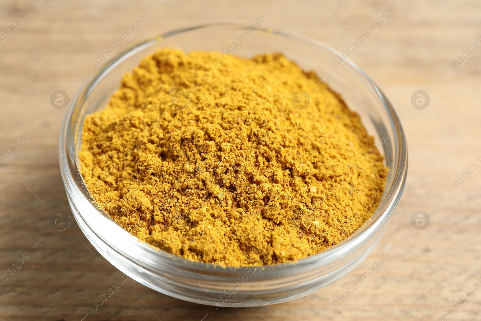 Photo of Curry powder in bowl on wooden table, closeup