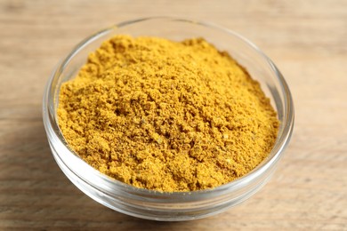 Photo of Curry powder in bowl on wooden table, closeup