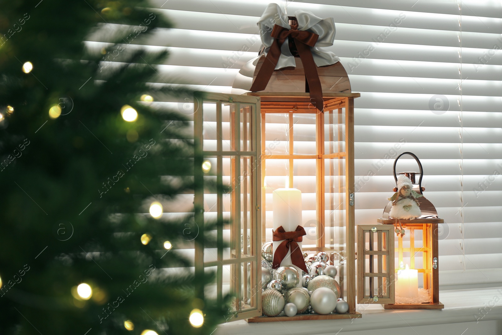 Photo of Wooden decorative lanterns with burning candles near Christmas tree indoors