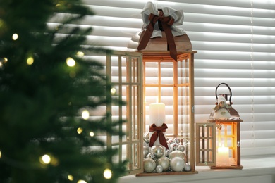 Wooden decorative lanterns with burning candles near Christmas tree indoors