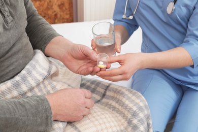 Photo of Nurse giving pills and water to senior patient in hospital ward, closeup