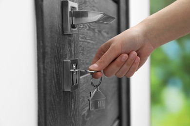 Photo of Woman unlocking door with key outdoors, closeup