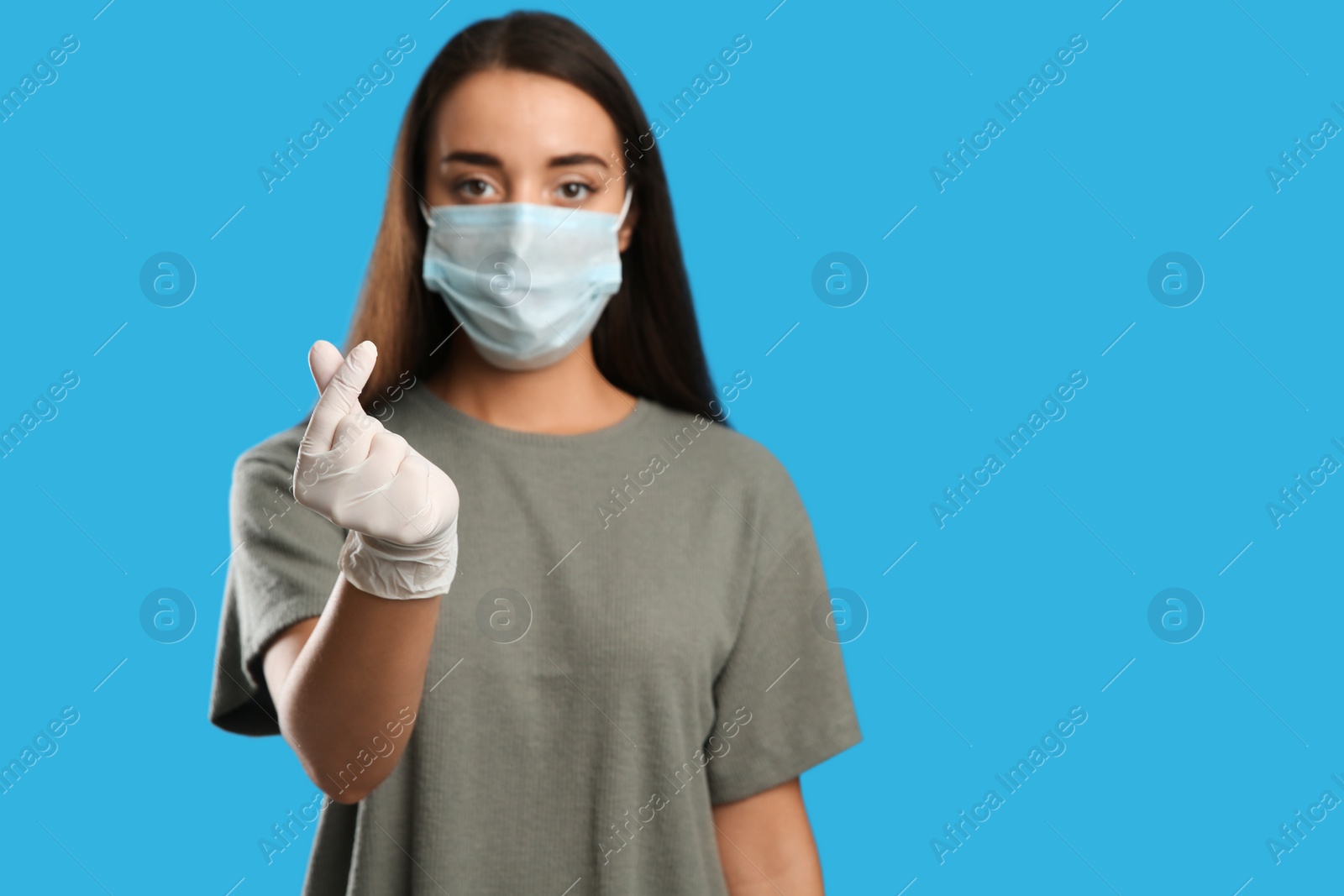 Photo of Woman in protective face mask and medical gloves showing heart gesture against blue background, focus on hand. Space for text