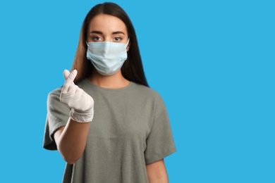 Photo of Woman in protective face mask and medical gloves showing heart gesture against blue background, focus on hand. Space for text