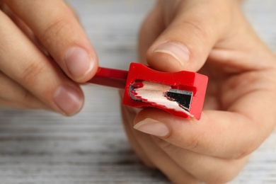 Photo of Woman sharpening pencil at wooden table, closeup