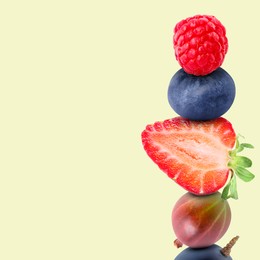 Stack of different fresh tasty berries on honeydew color background, space for text