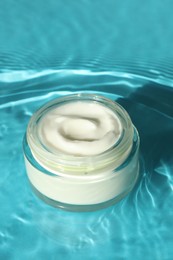 Jar with moisturizing cream in water on light blue background