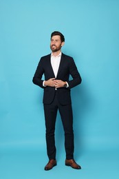 Handsome bearded man in suit looking away on light blue background