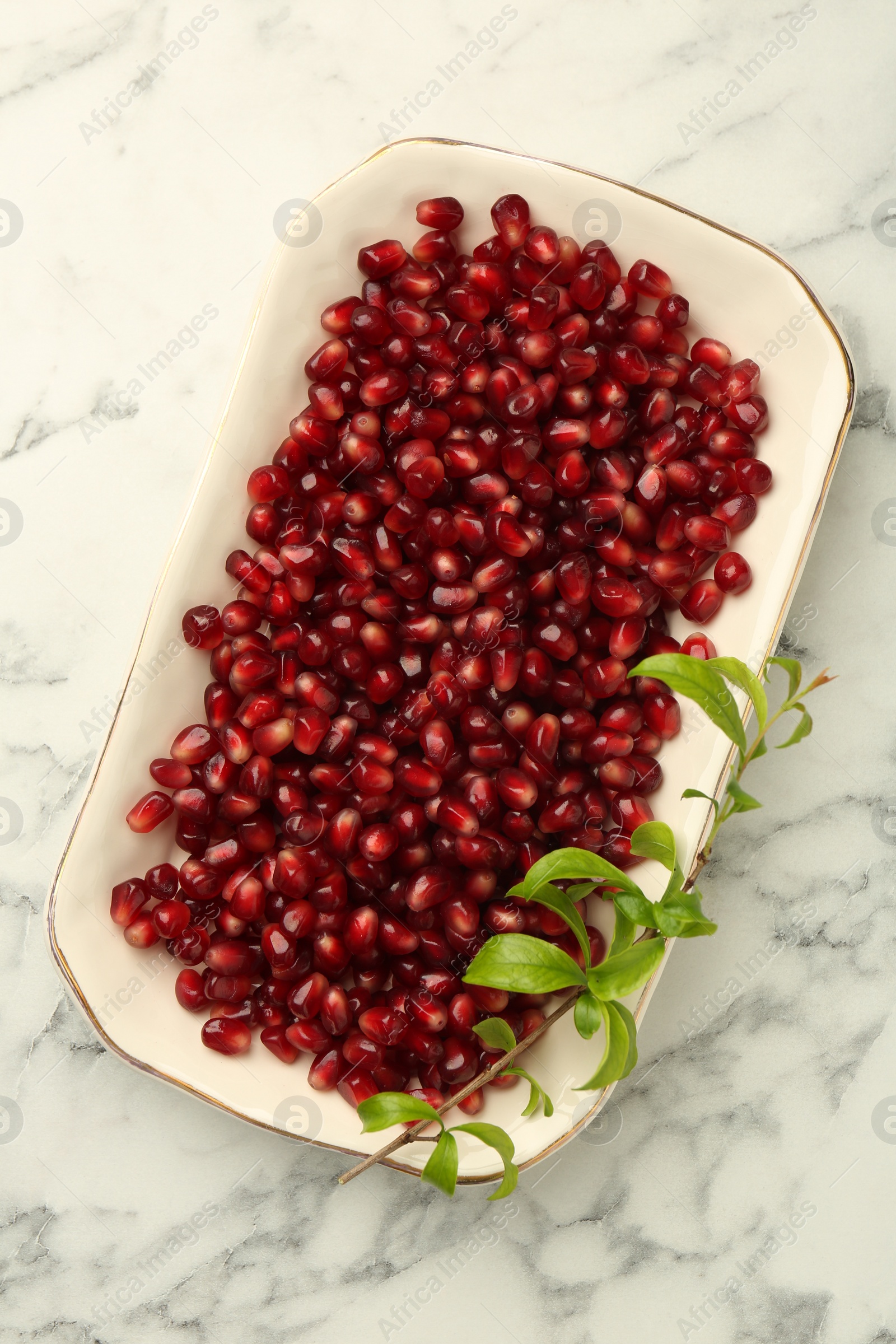 Photo of Ripe juicy pomegranate grains and green leaves on white marble table, top view