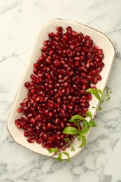 Photo of Ripe juicy pomegranate grains and green leaves on white marble table, top view