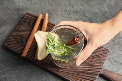 Photo of Woman holding glass cocktail with rosemary on table, closeup