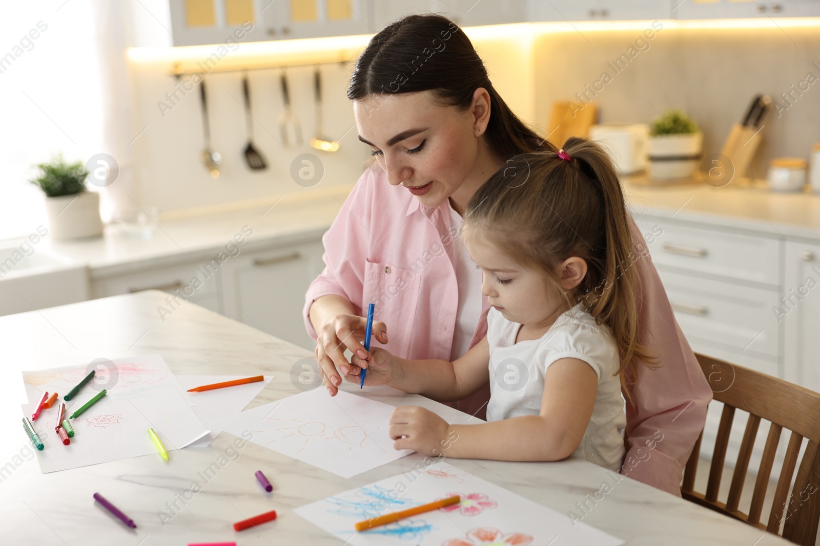 Photo of Mother and her little daughter drawing with colorful markers at table in kitchen