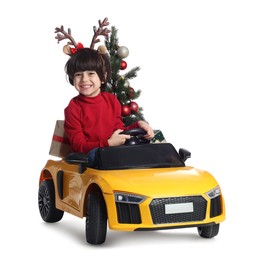Photo of Cute little boy with Christmas tree and gift box driving children's electric toy car on white background