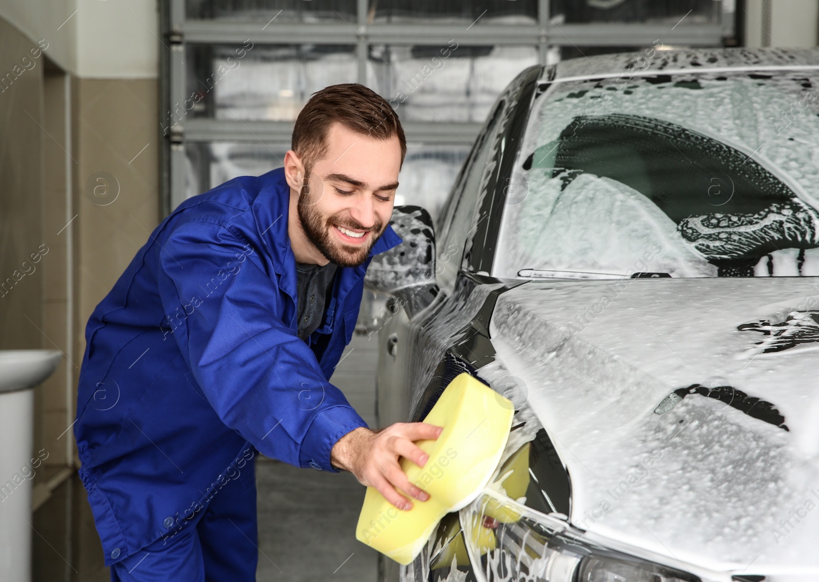 Photo of Worker cleaning automobile with sponge at professional car wash