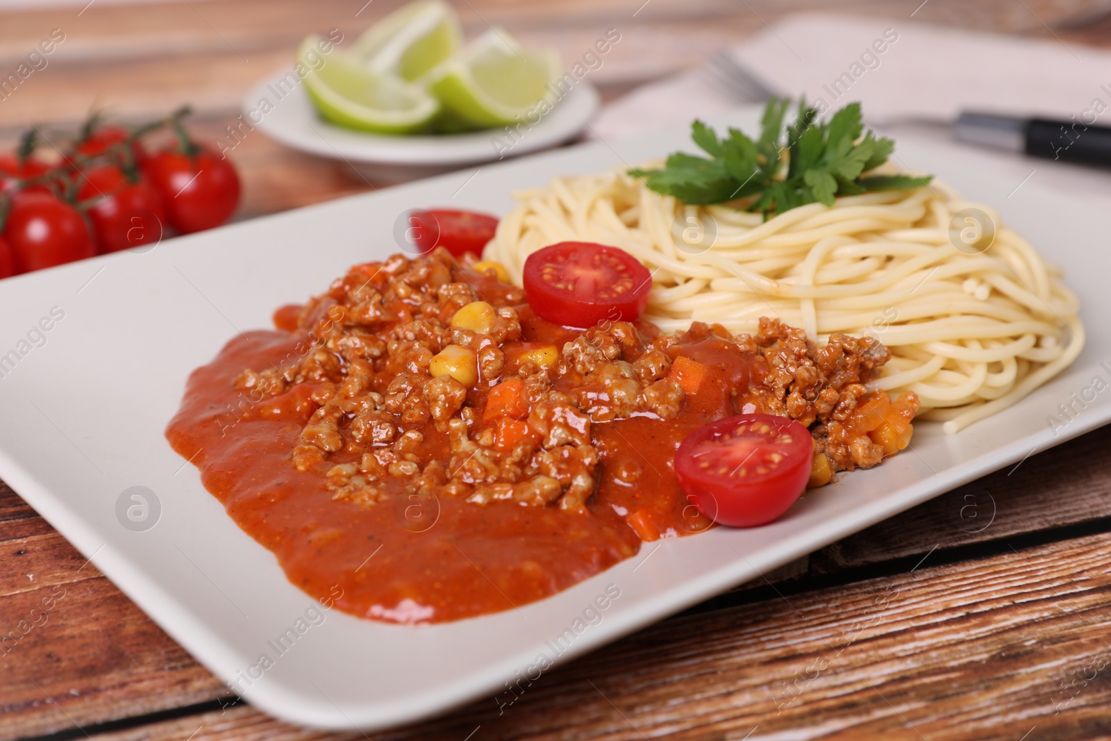 Photo of Tasty dish with fried minced meat, spaghetti, carrot, corn and cherry tomato served on wooden table, closeup