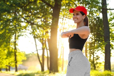 Young woman doing morning exercise in park, space for text