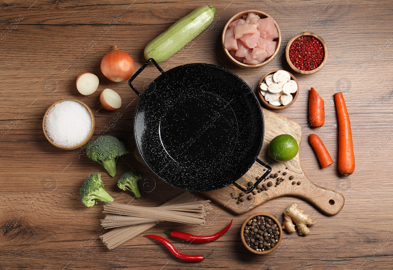 Photo of Empty iron wok surrounded by raw ingredients on wooden table, flat lay